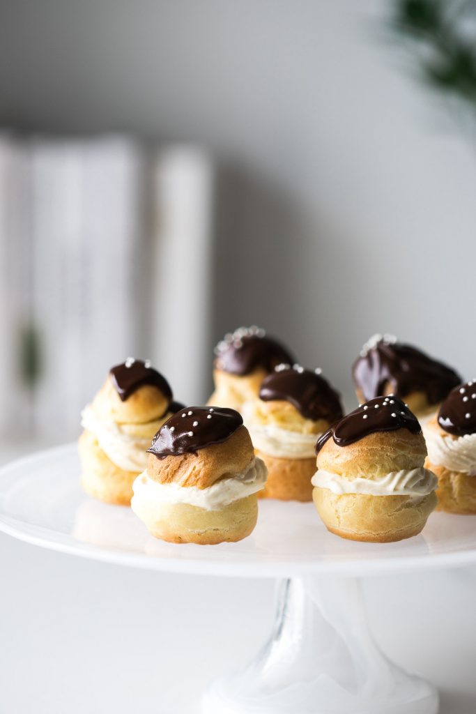 Several finished Choux à la Crème sitting on a cake stand