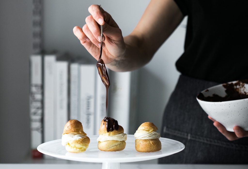 Shot of woman drizzling chocolate ganache onto Choux à la Crème