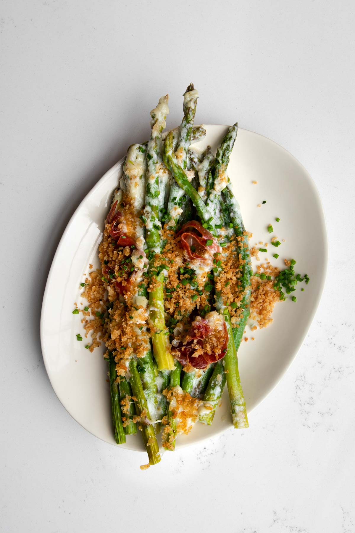 Asparagus au gratin with prosciutto served on an oval plate.