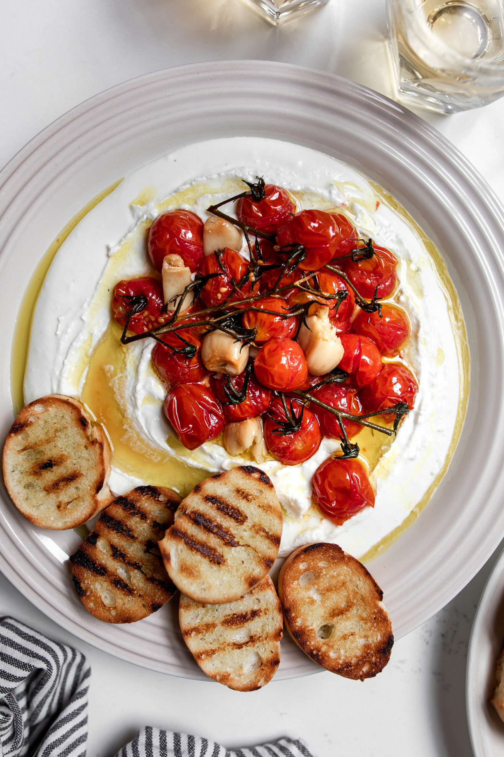 Confit tomatoes on whipped cheese with grilled baguette on a plate.