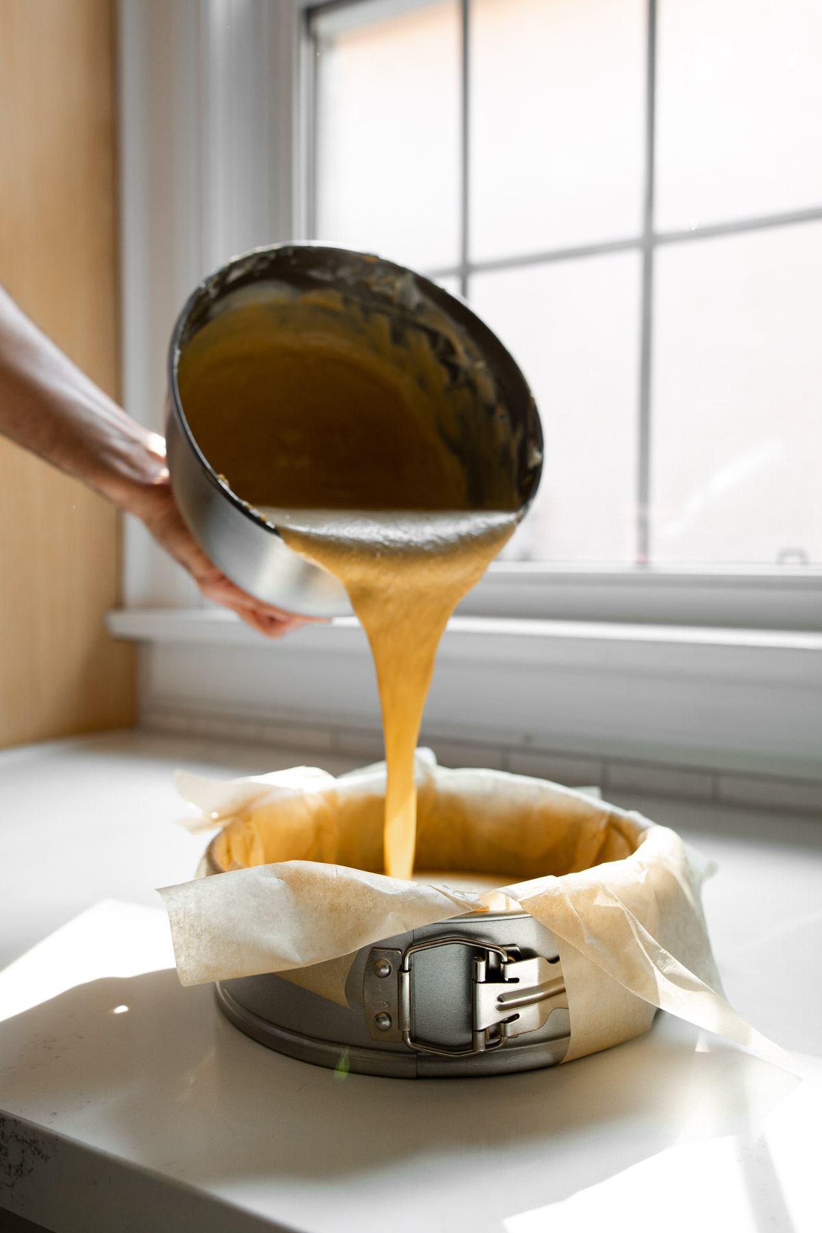 Pouring batter into a parchment-lined springform pan.